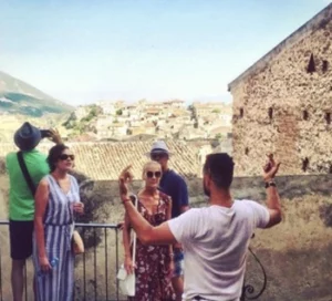 A tour guide passionately explaining the historical and cultural significance of a scenic village in Calabria, with a group of visitors engaged in the experience against a picturesque backdrop of terracotta rooftops and rolling hills.